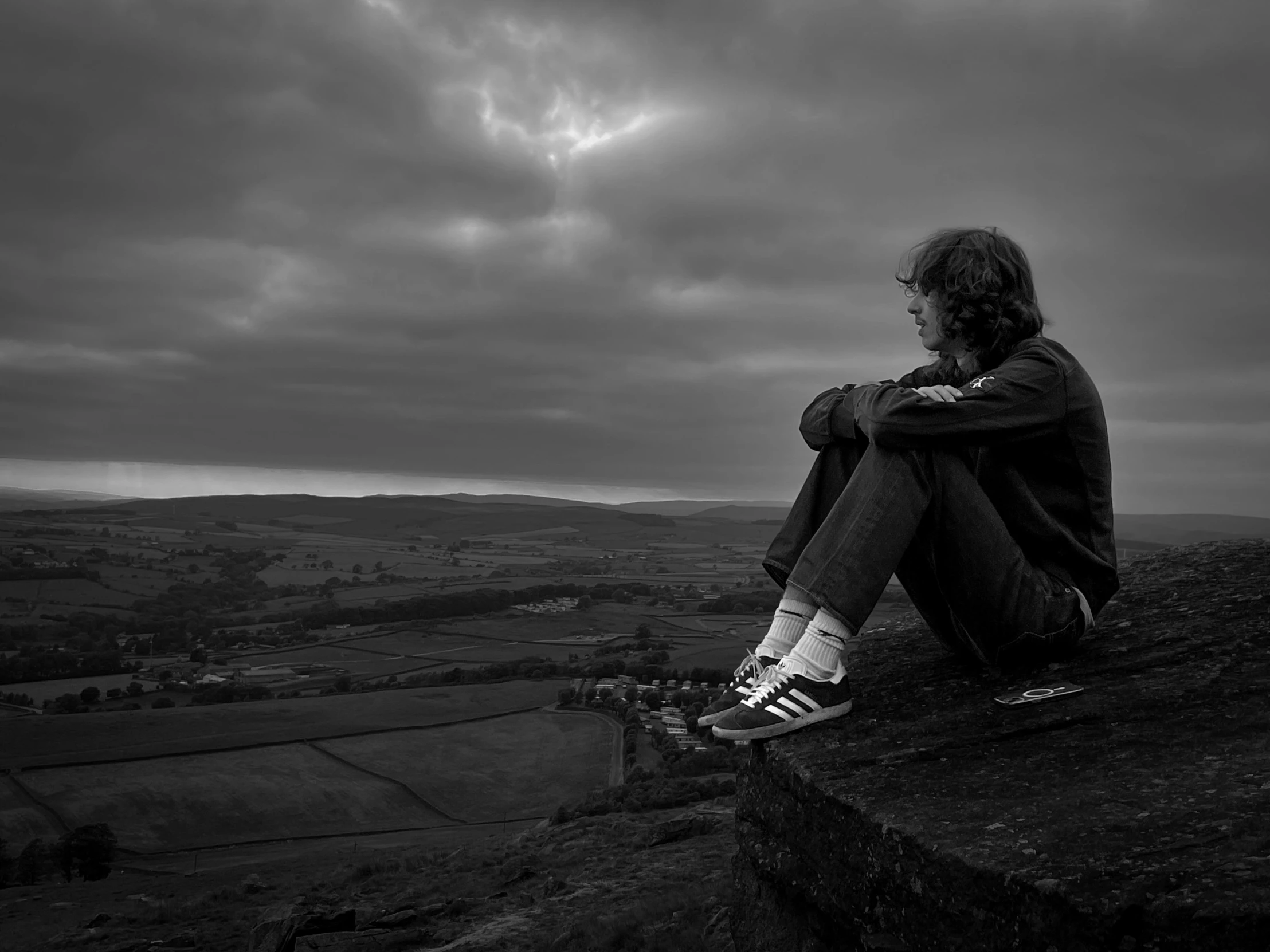 man sits at top of rock looking out to hills