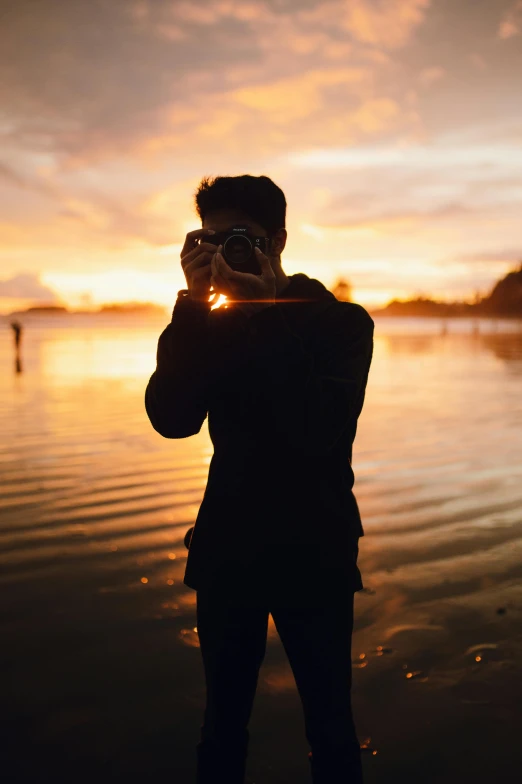 a person standing in front of the water taking a picture with his camera