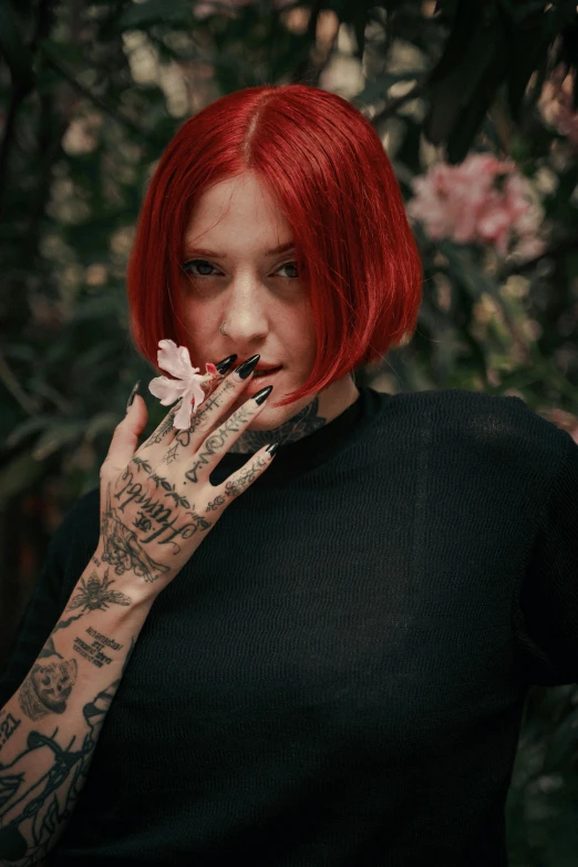 a woman with red hair with a black shirt holding up a flower