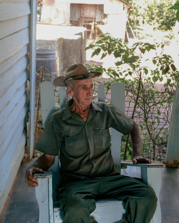 an old man sitting in a rocking chair wearing a hat