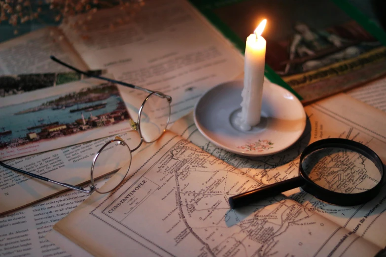 an open newspaper on a table next to a candle with some glasses