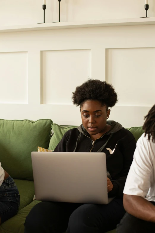 three people sit on a couch with laptops