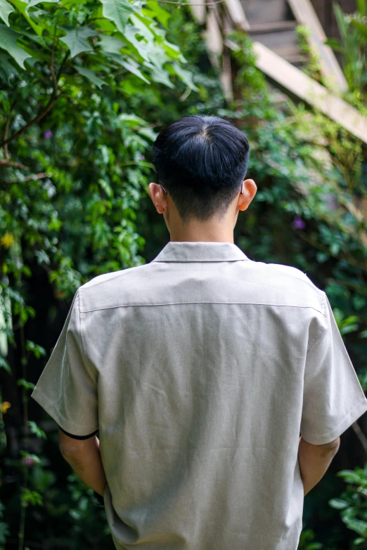 a man in a shirt stands in front of some trees and plants