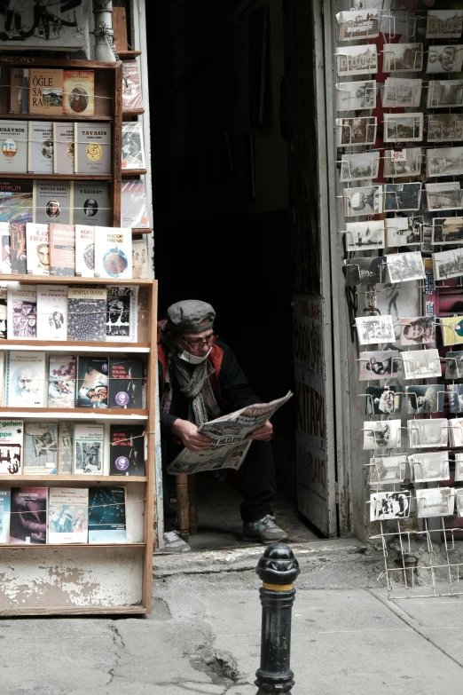 a person sitting in a door of a shop reading a newspaper