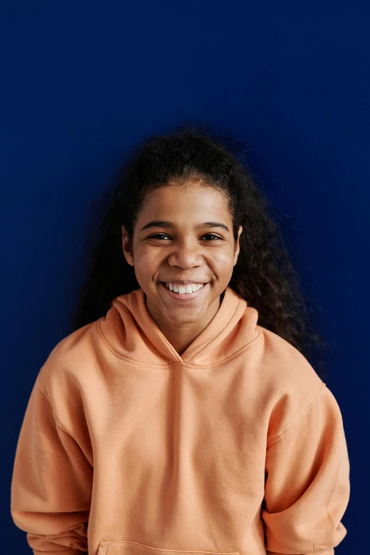 an indian woman poses in front of a blue wall wearing a bright sweatshirt