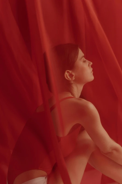 a woman sitting under a red cloth on top of a bed