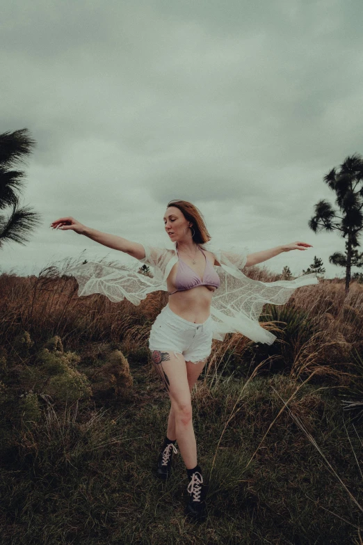 a woman is posing with a mesh shawl in the grass