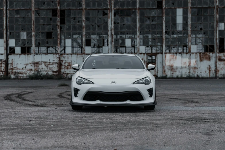 the white car is parked in front of a rusty building