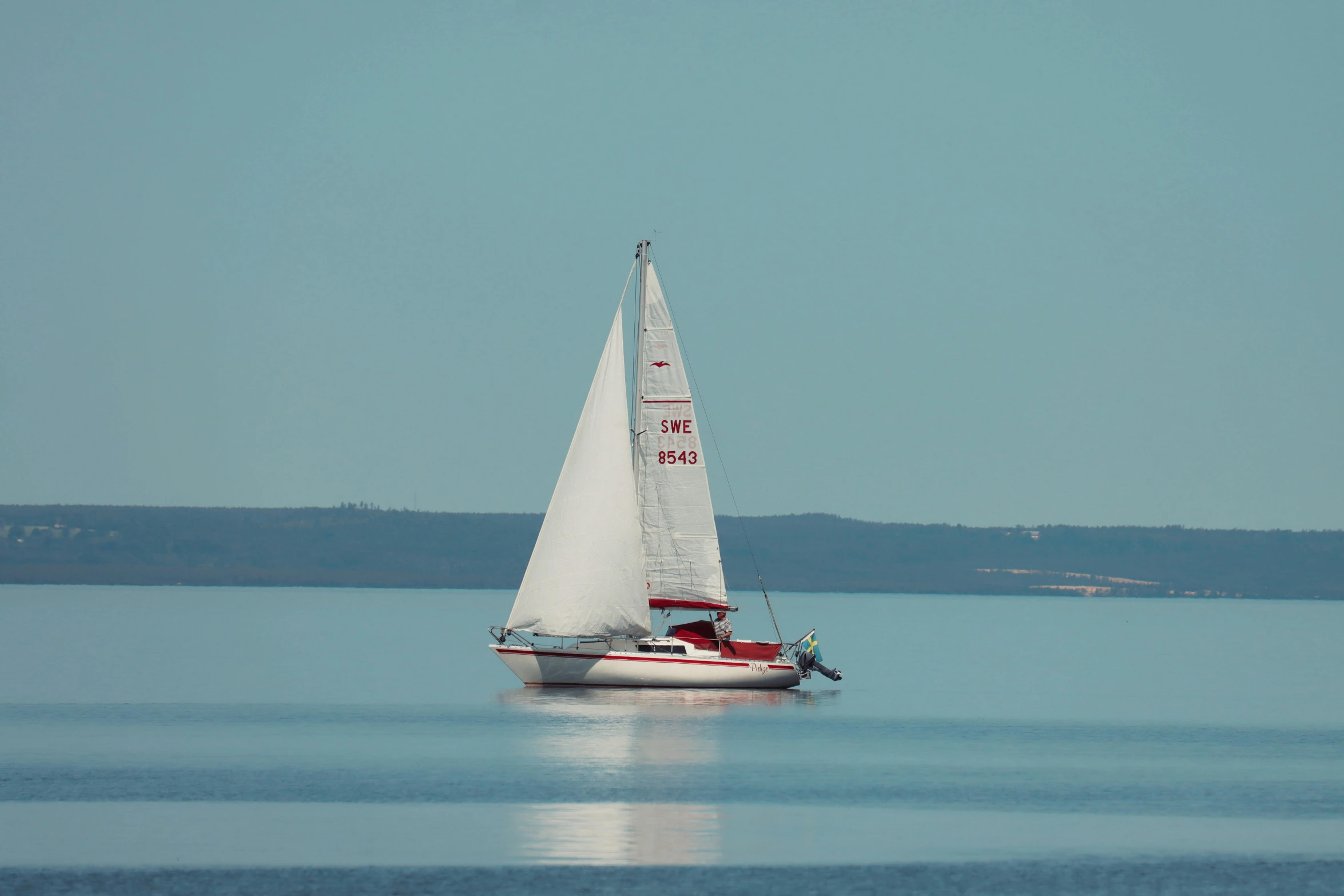 the boat is white with red sails on the water