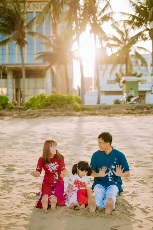 a couple and their two children sit on the sand at the beach with their hands together