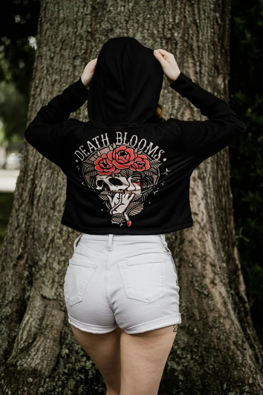 a women standing in front of a tree, wearing a sweatshirt that says death blooms