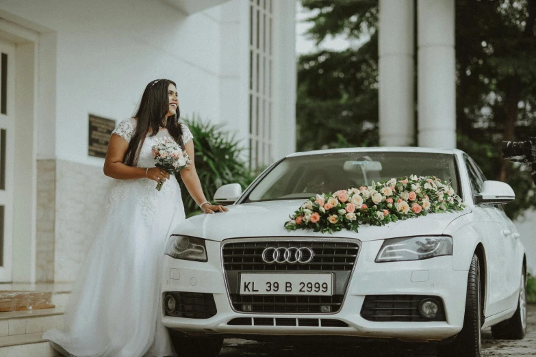 the bride is standing beside a white car with flowers