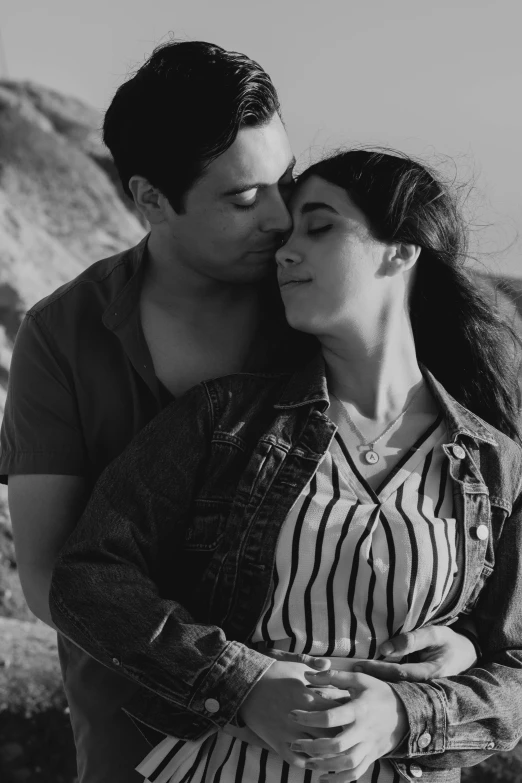 a young man kisses the forehead of a woman in front of some rocky terrain