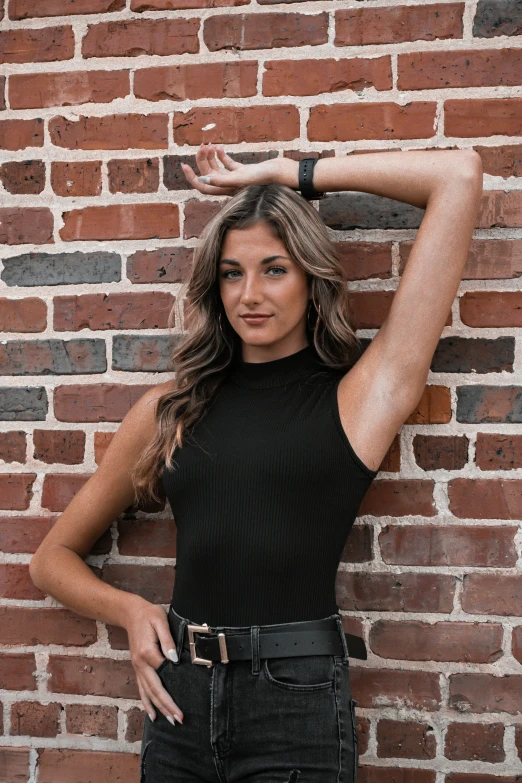 a woman standing against a brick wall with her arms on her head