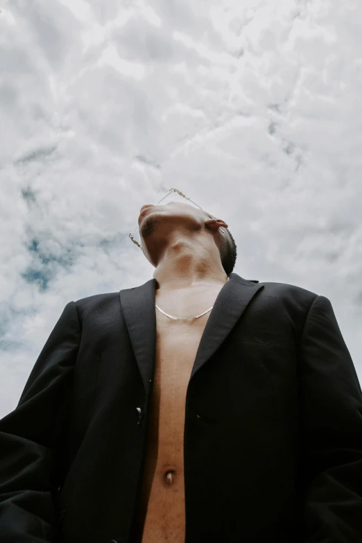 a shirtless person in black jacket standing under a cloudy sky