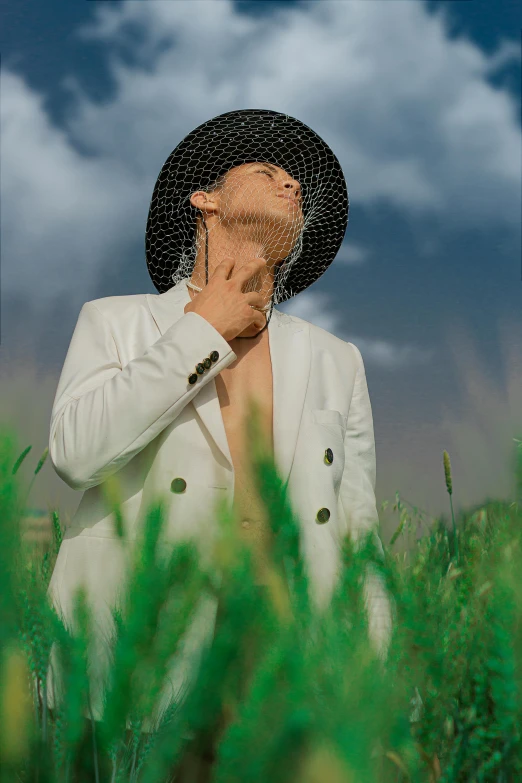 a man covers his face with a hat as he walks through some tall grass