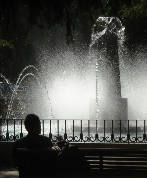 a person sits alone on a bench and looks at a fountain