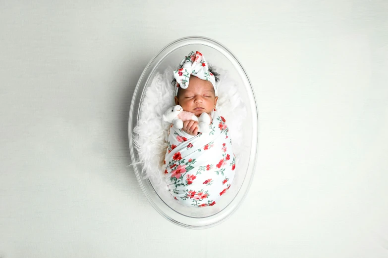 newborn baby in white flowered blanket on white wall