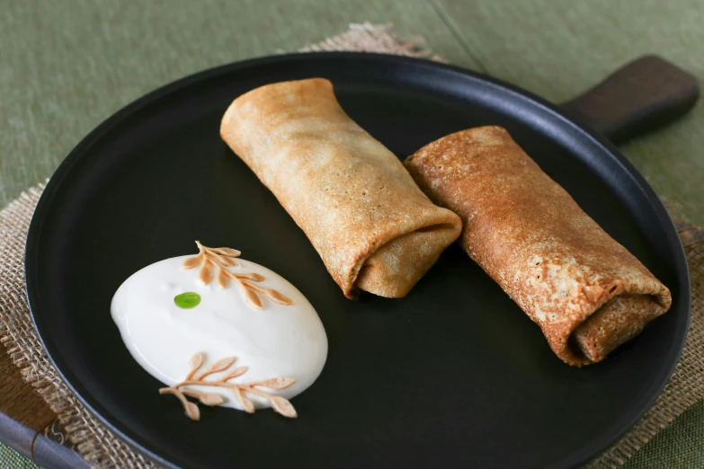 two meat rolls and an egg yogurt are sitting on a black plate