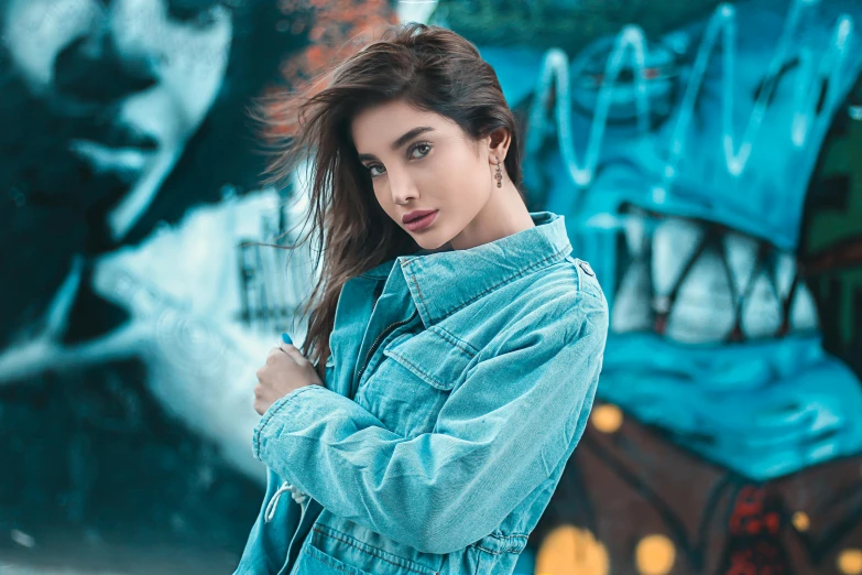 a woman in a blue jacket and jeans stands near graffiti