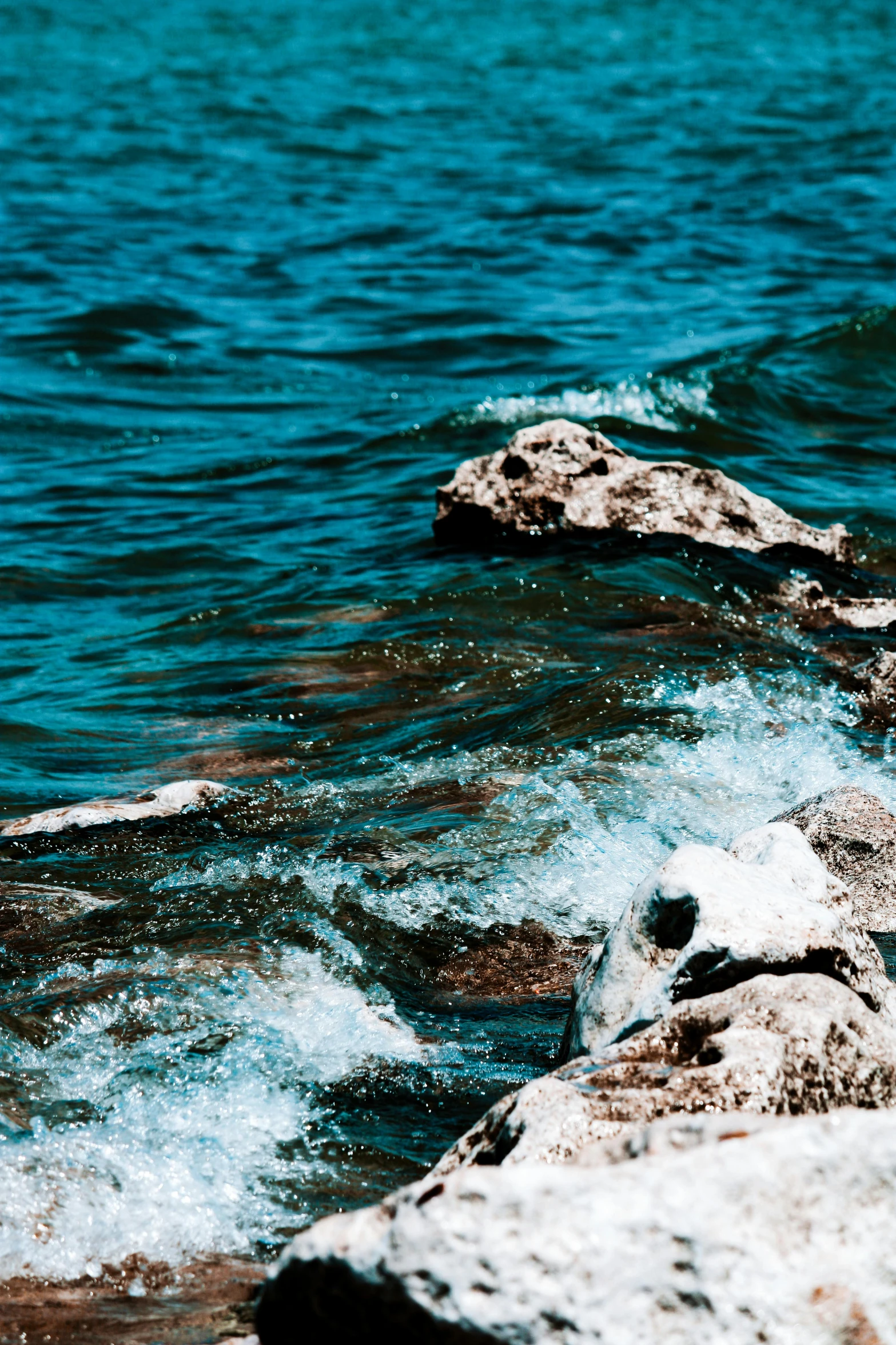 a person sitting on a rock on the shore of a lake with clear blue water