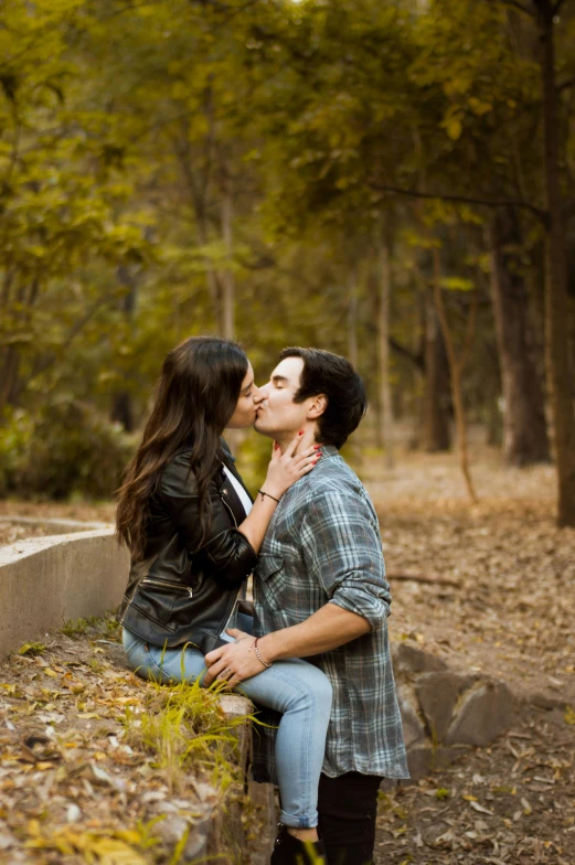 an attractive couple kissing each other in the woods