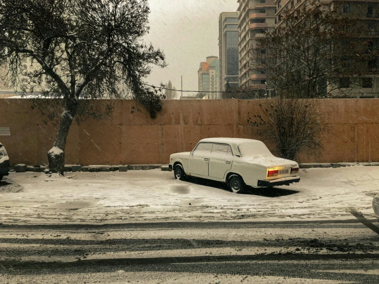 two cars sitting parked in the snow in front of a fence