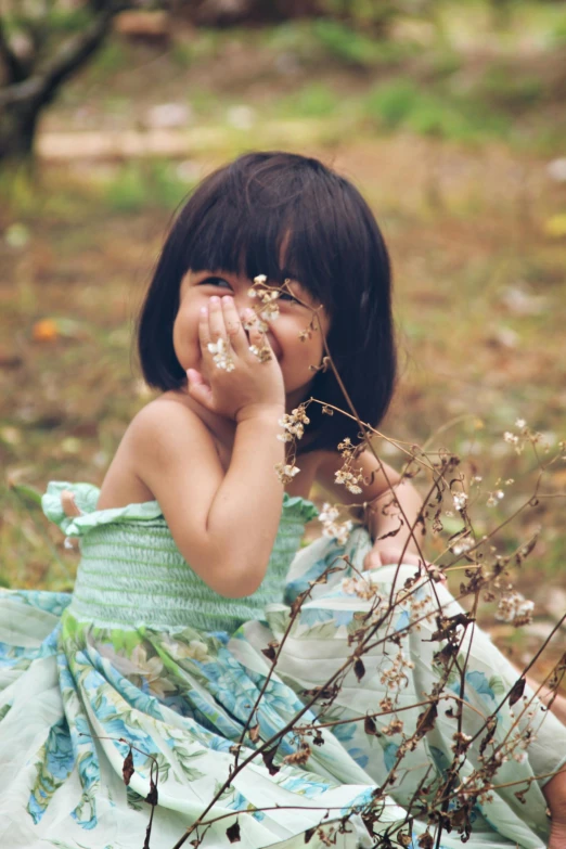 a little girl sitting on the ground next to some flowers