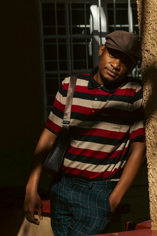 a man leaning against a wall wearing striped shirt