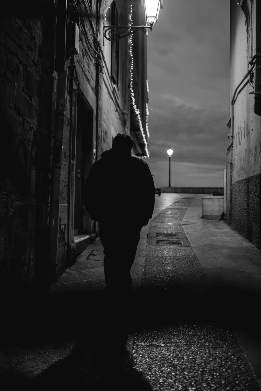 a man walks down the side of an alley in black and white