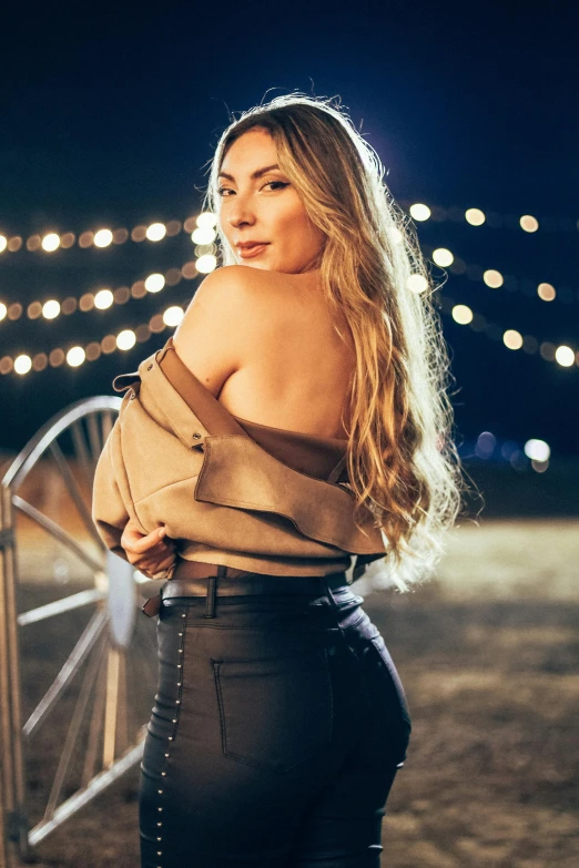 a woman poses against a fence with lights in the background