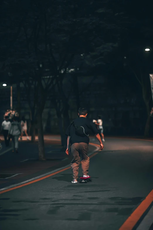 skateboarder riding on the pavement while pedestrians pass by at night