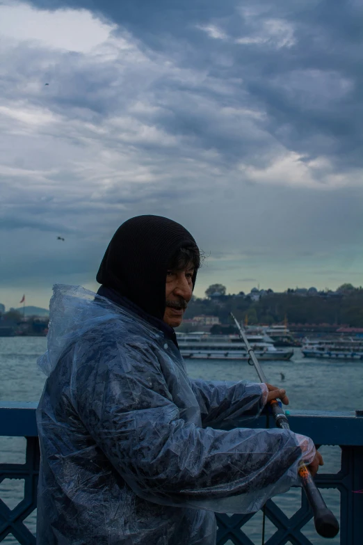 the man has on a raincoat, holding a fishing rod