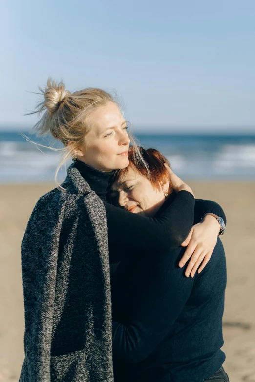 two people standing on the beach hugging each other