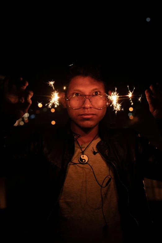 person wearing glasses, and holding fireworks in the dark