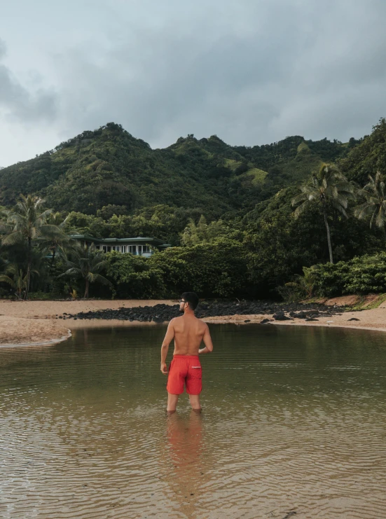 a man wading in shallow water while holding onto his red and black life jacket