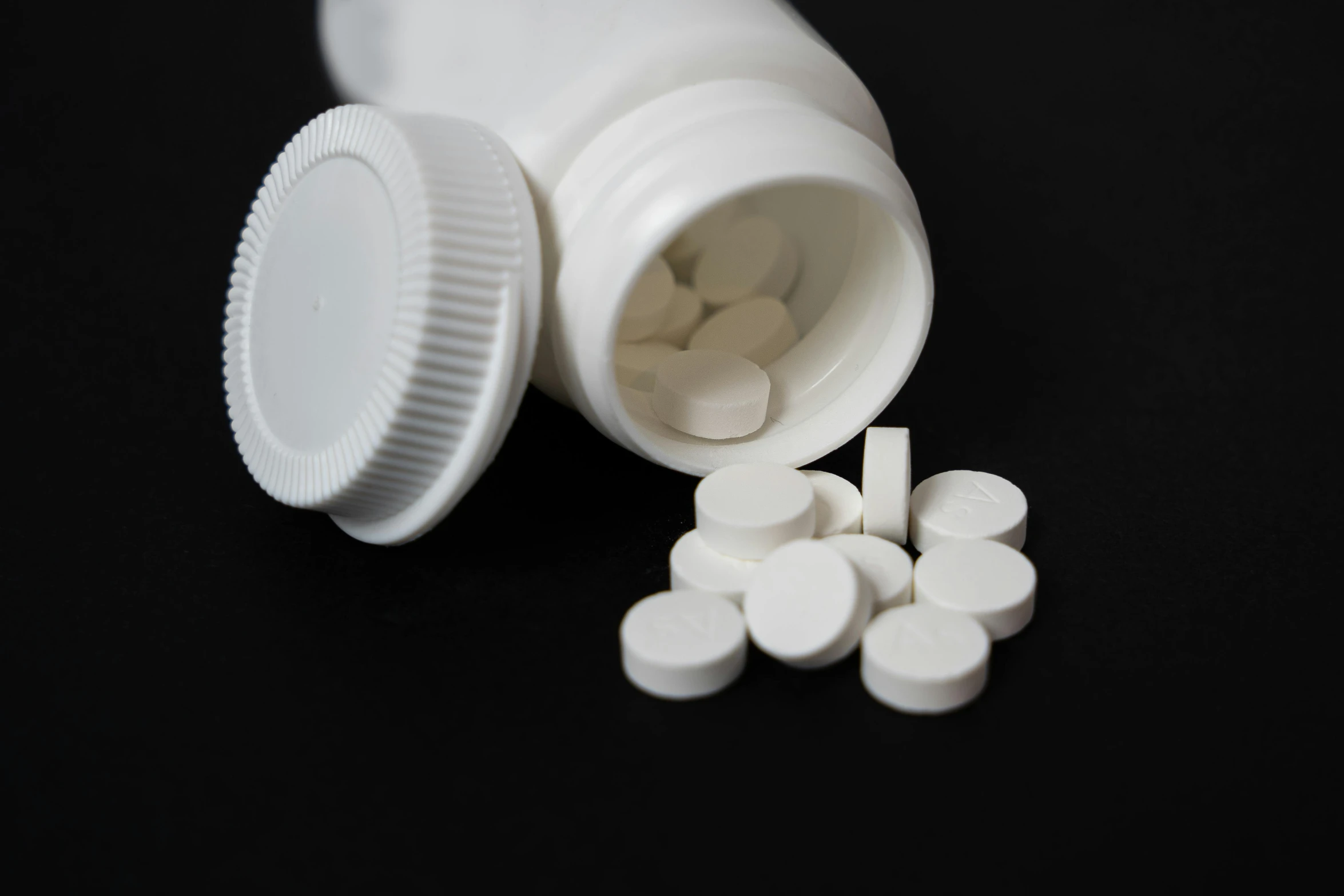 white pills spilling out from a white bottle onto black table