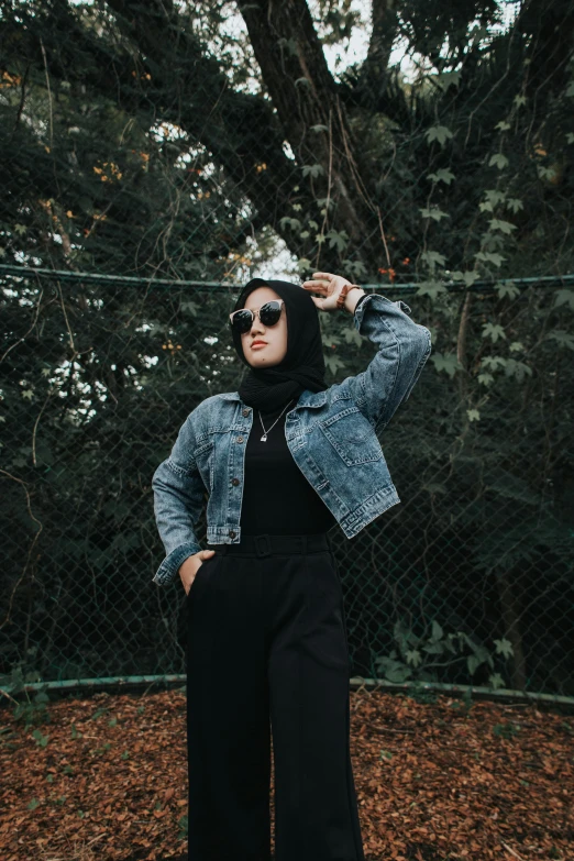 a woman in sunglasses and a jacket poses outside by a fence