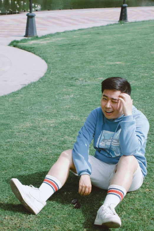 a man in blue sweatshirt sitting in grass talking on cell phone