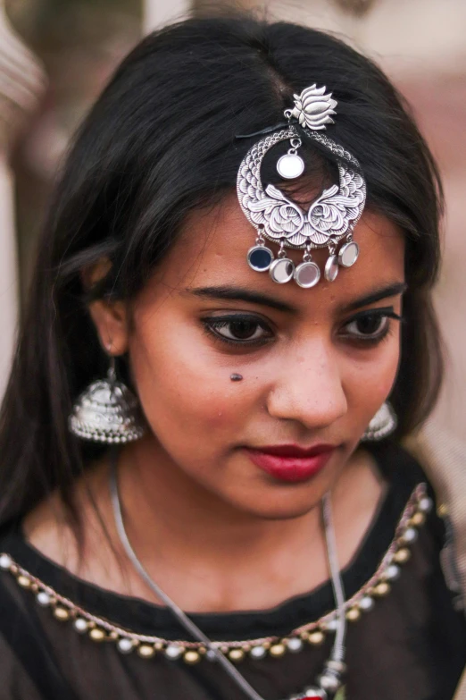 the woman wearing an elaborate necklace and ear rings is looking to her right