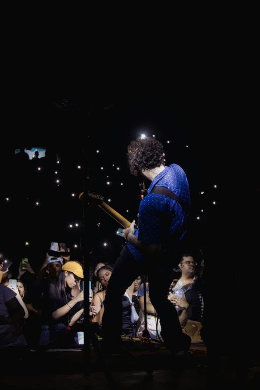 man playing a guitar at night, performing in front of a crowd