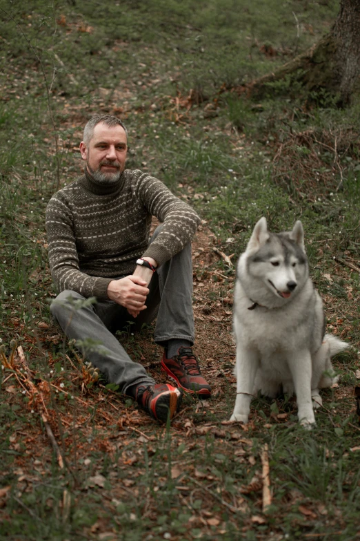 a man sits in the grass with his husky