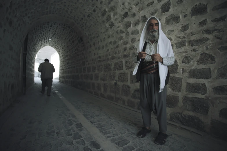 man standing in dark alley with head covering looking at phone