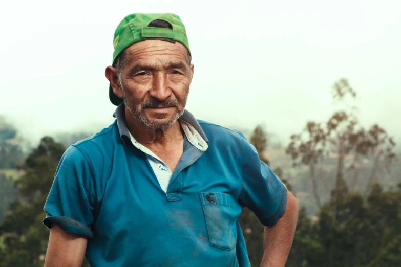 an elderly man wears a hat on his head while standing next to a hill