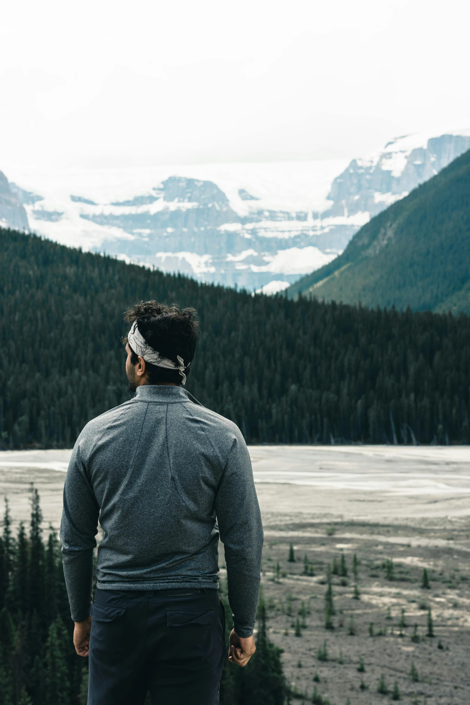 a man in grey shirt looking over snowy mountains