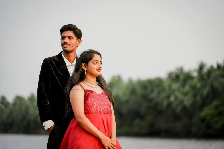 a young couple standing together in front of some water