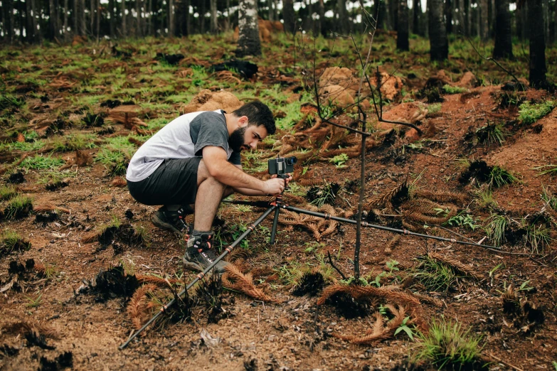 a man is crouched over with a camera on a wooden pole in the woods