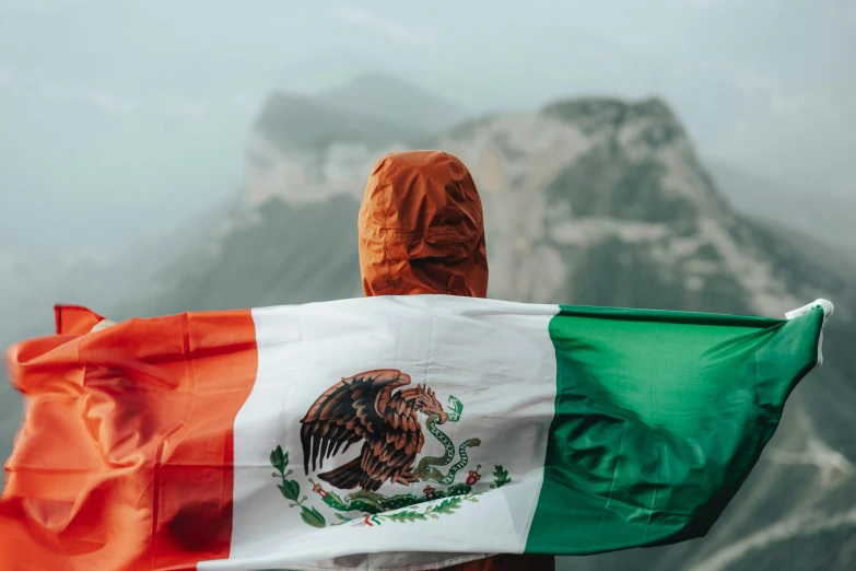 a mexican man holding up a flag on a mountain