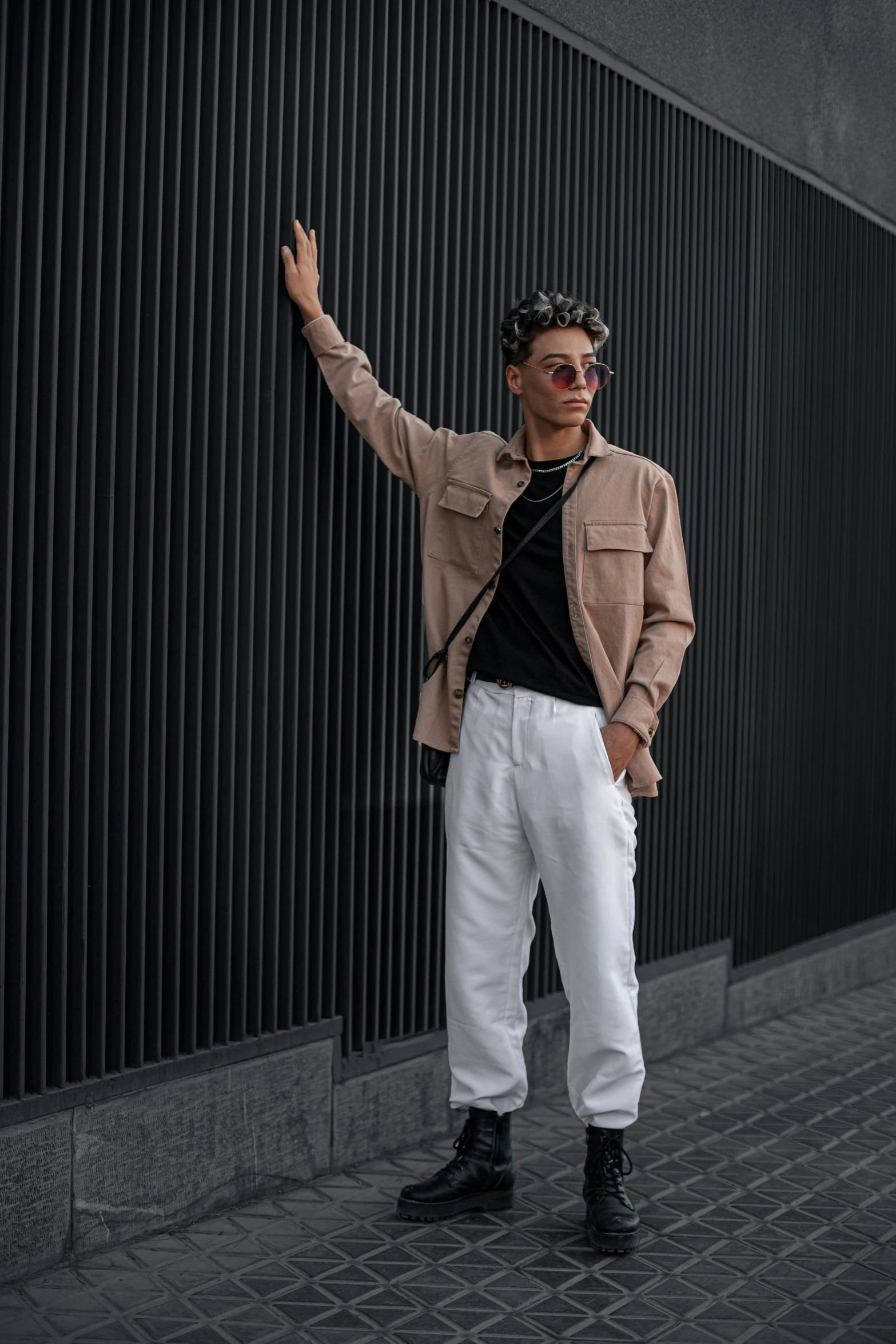 a young man leaning against a wall wearing pants and a jacket