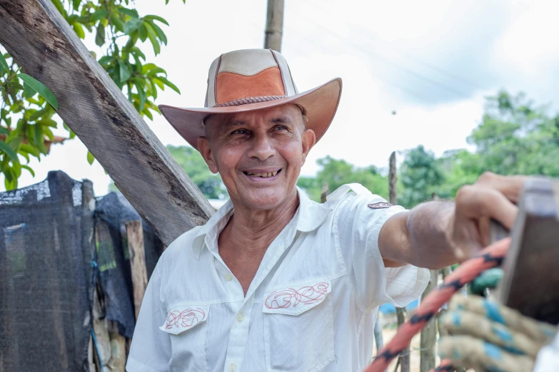 a smiling man in a cowboy hat holds a camera